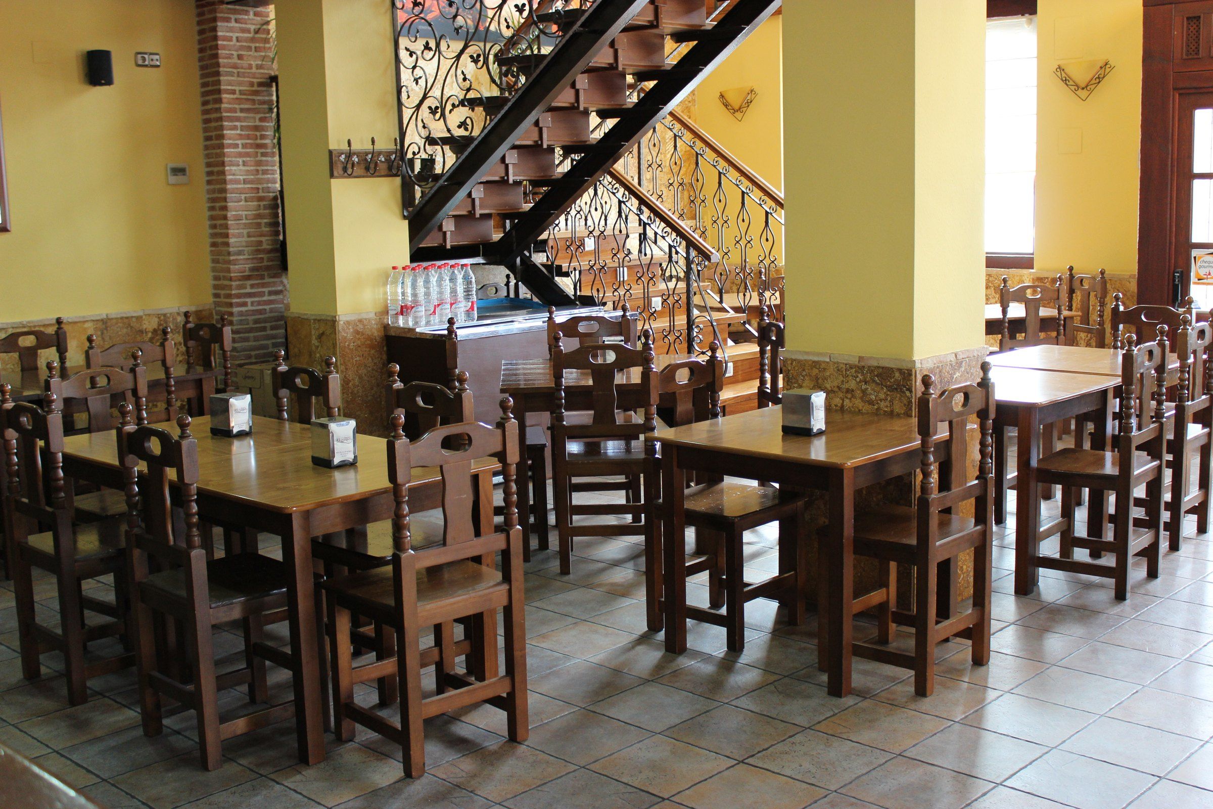 Comedor de la planta baja con mesas de madera y la escalera de forja al salón
