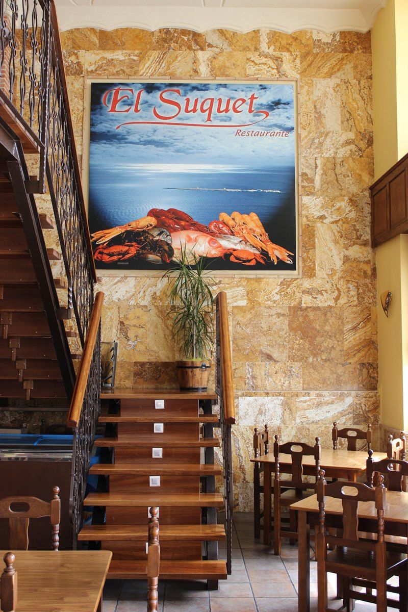 Escalera de madera con cuadro de mariscos y el cartel de El Suquet