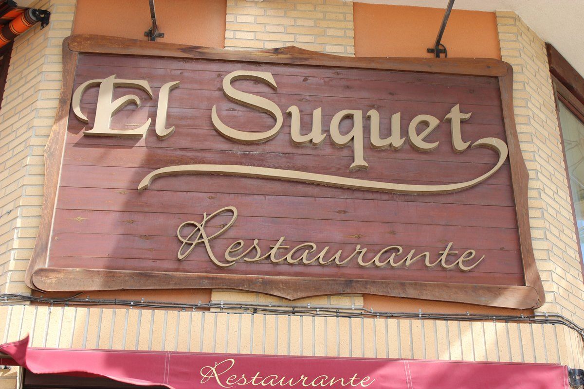 Rótulo de madera de El Suquet Restaurante sobre el toldo de la entrada